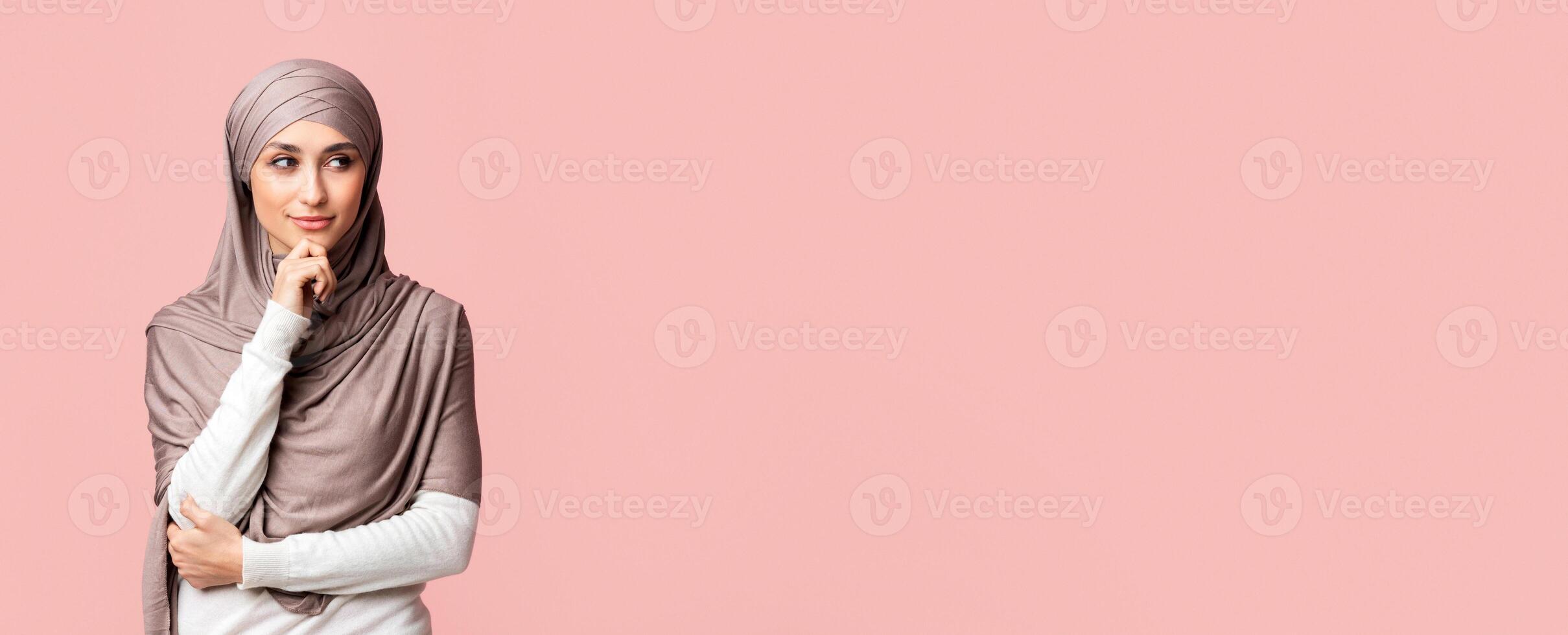 Making plans. Portrait of pensive arabic woman in hijab thinking about something, touching chin and looking aside at copy space over pink background photo