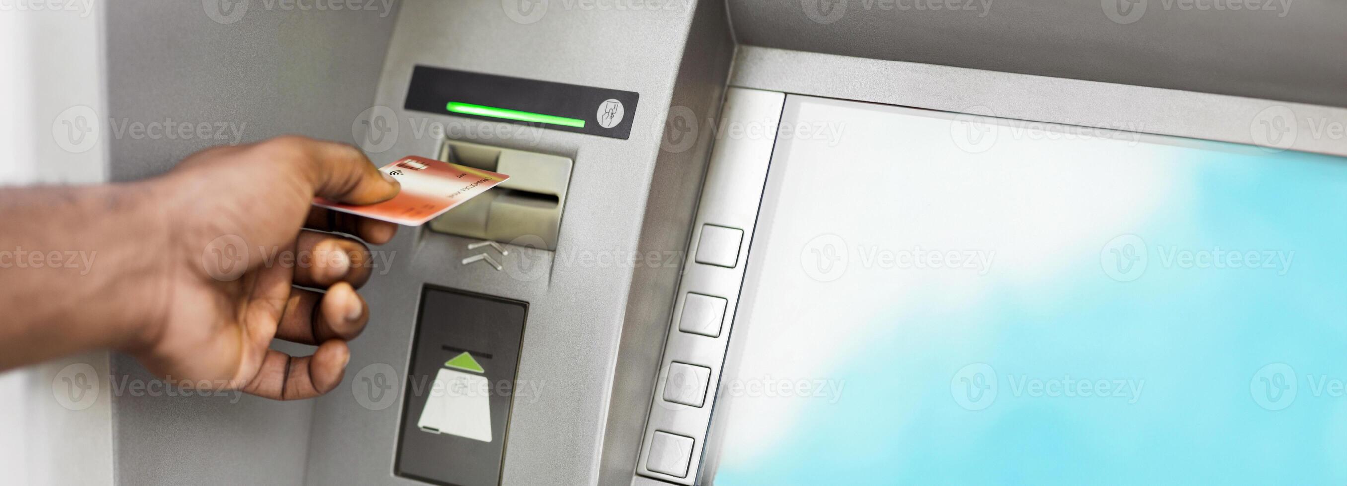 Close up of black man using ATM with gold credit card, panorama, copy space photo