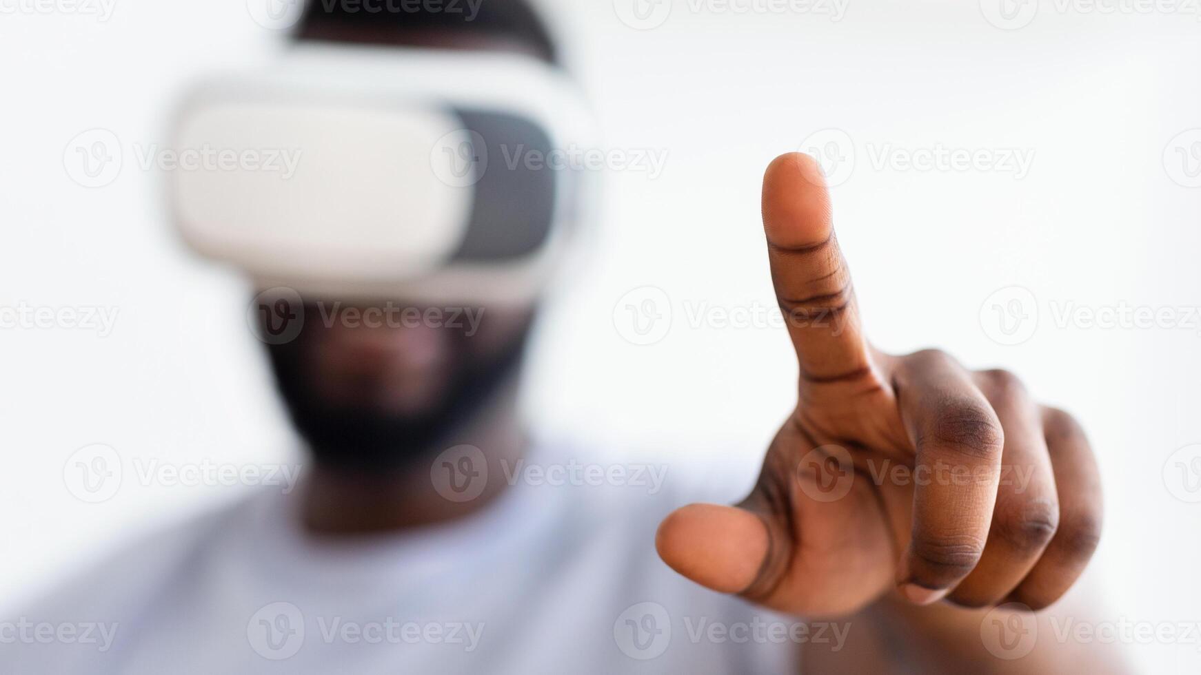 A close-up photo shows African American man wearing a virtual reality headset, his right hand extended forward, with his index finger pointing up as he interacts with digital content.