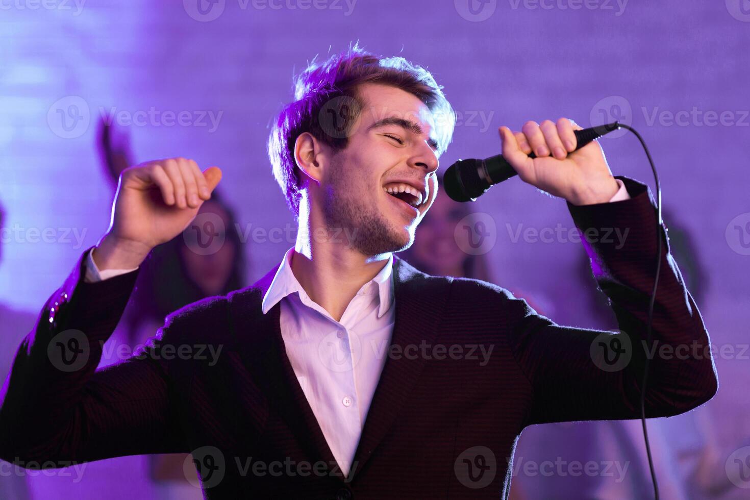 Millennial Guy Singing Song Holding Microphone At Karaoke Night Party Indoor. Low Light photo