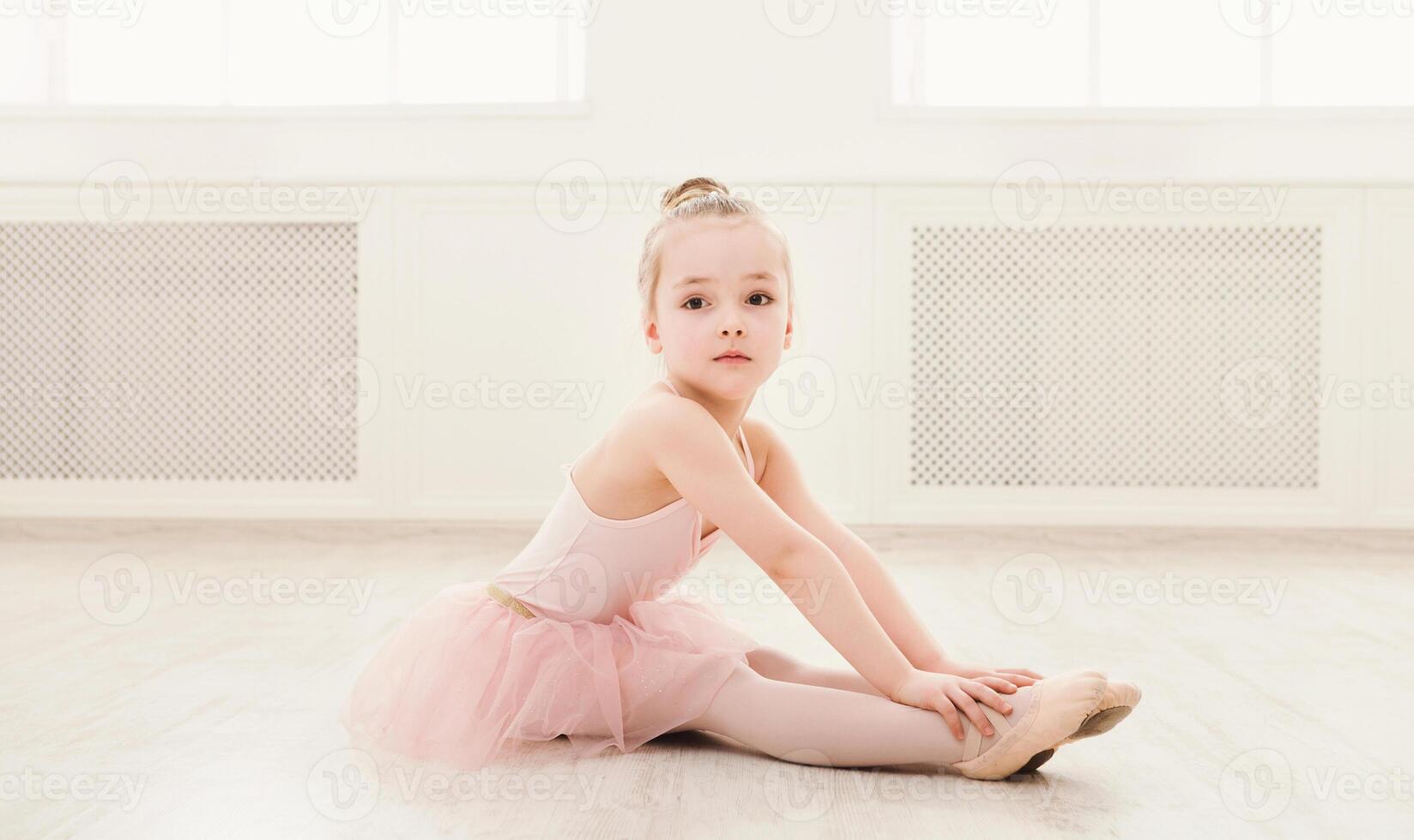 Portrait of little ballerina on floor, copy space. Smiling baby girl dreaming to become professional ballet dancer, classical dance school photo