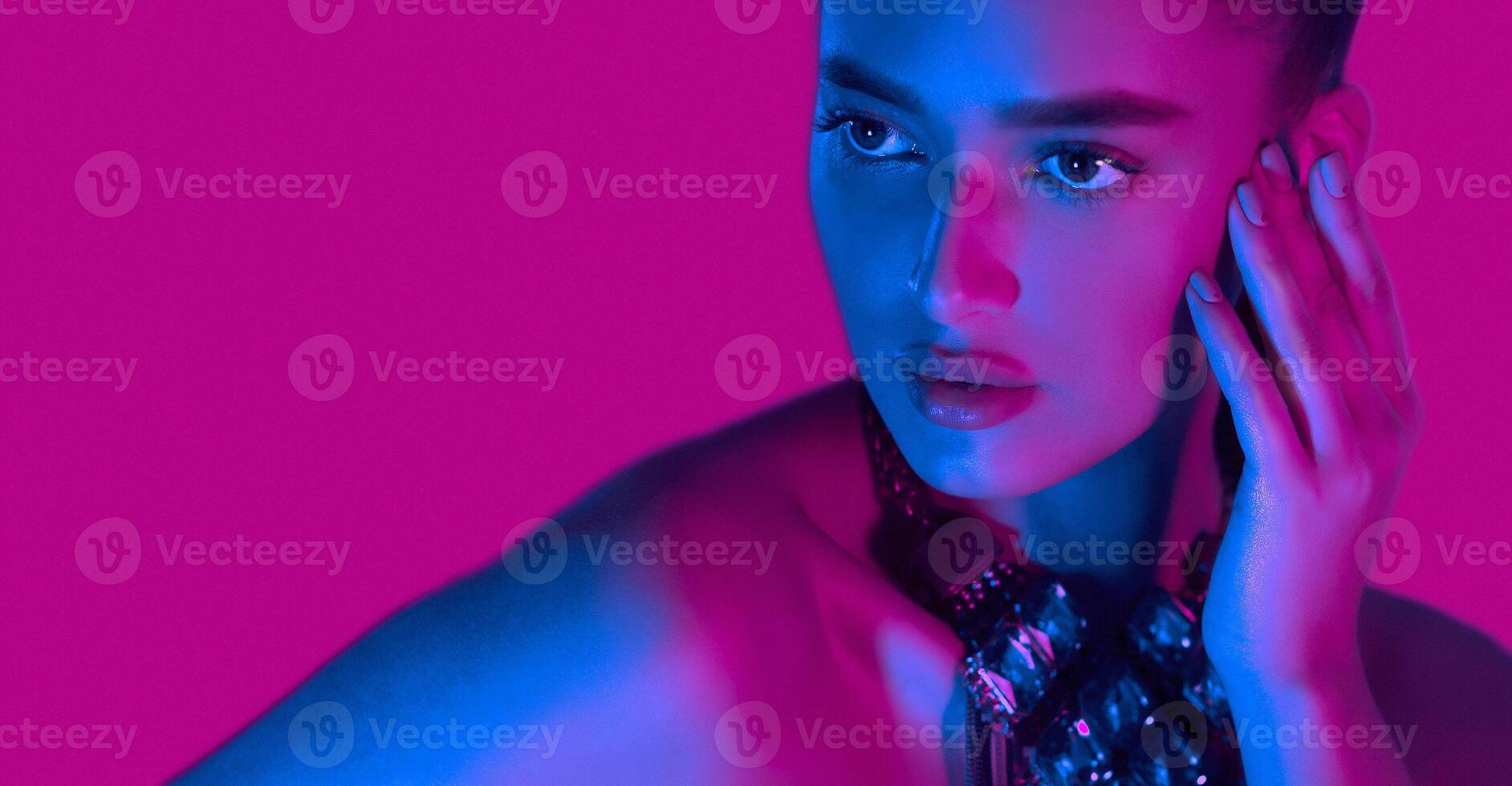 A woman is standing in a confident pose in front of a vibrant pink background. Her posture is elegant and graceful as she gazes directly at the camera. The pink backdrop adds a pop of color photo