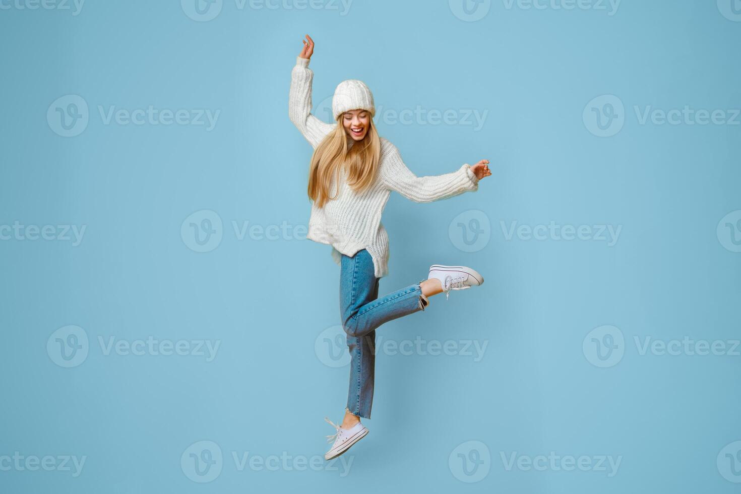 Cheerful blonde girl in warm clothes dancing and jumping in the air, yellow background photo