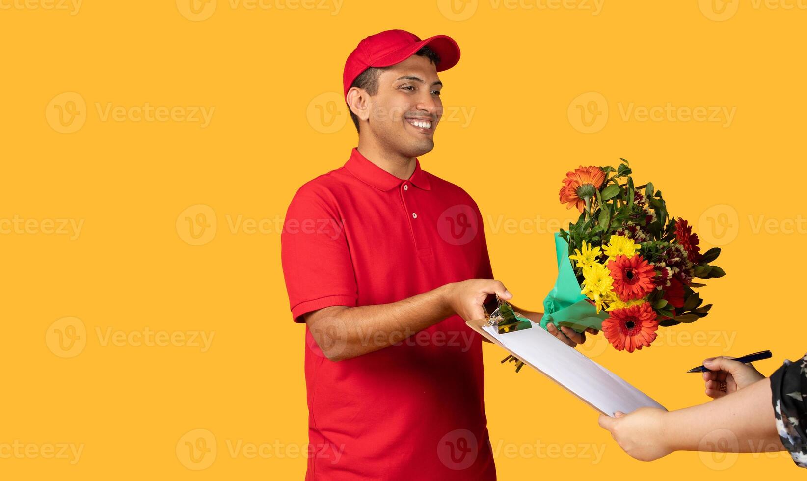 Delivery man is extending a bouquet of flowers to a woman. The woman is reaching out to accept the bouquet. They are standing isolated on yellow background photo