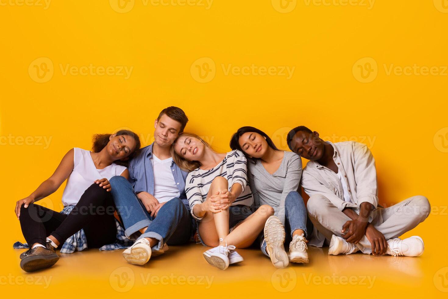 Tired multiracial classmates sitting on floor and sleeping after exams over yellow background photo