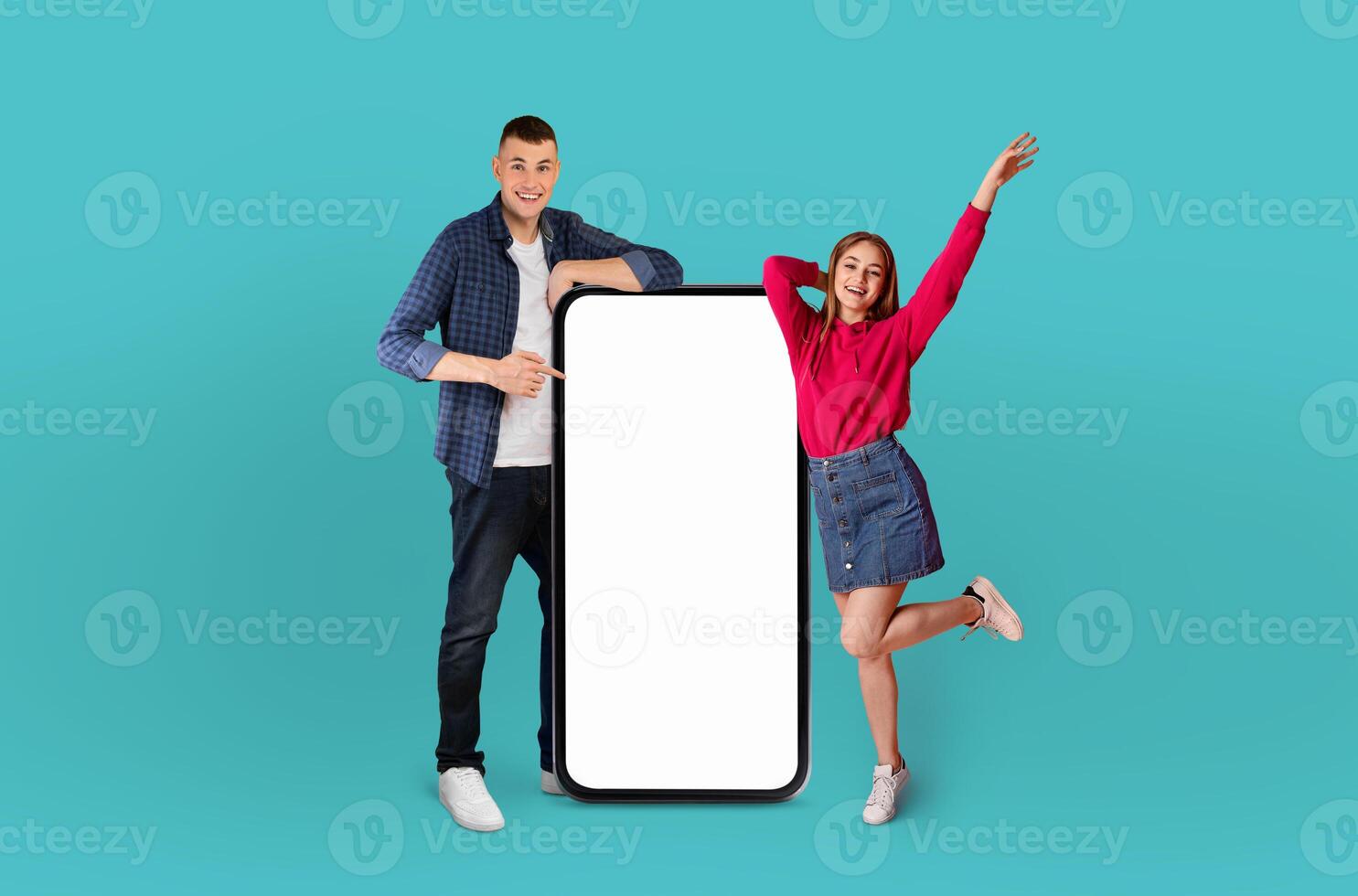 Emotional man and a woman are standing together holding a blank white phone in their hands. The background is a plain blue color, providing a simple backdrop for the subjects. photo