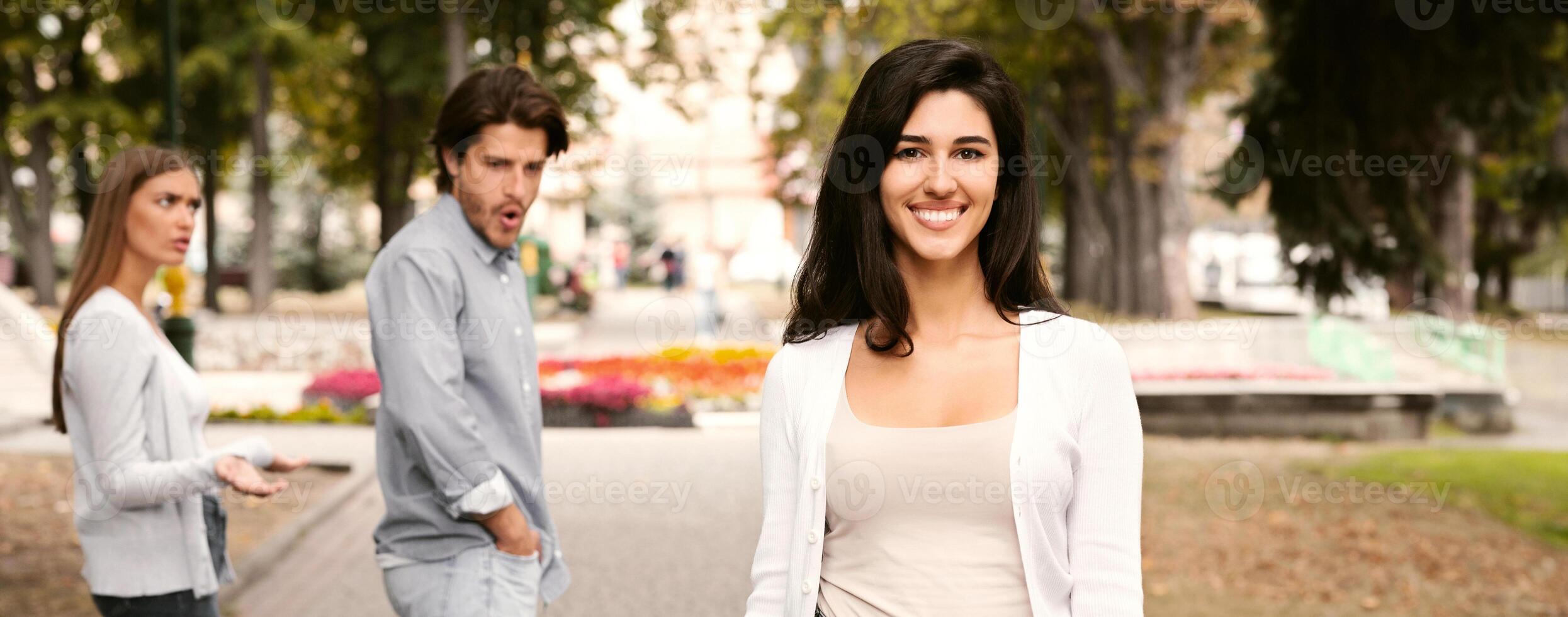 Jealousy Concept. Man Being Distracted By Attractive Girl Walking With Jealous Girlfriend Having Date In Park. Selective Focus photo