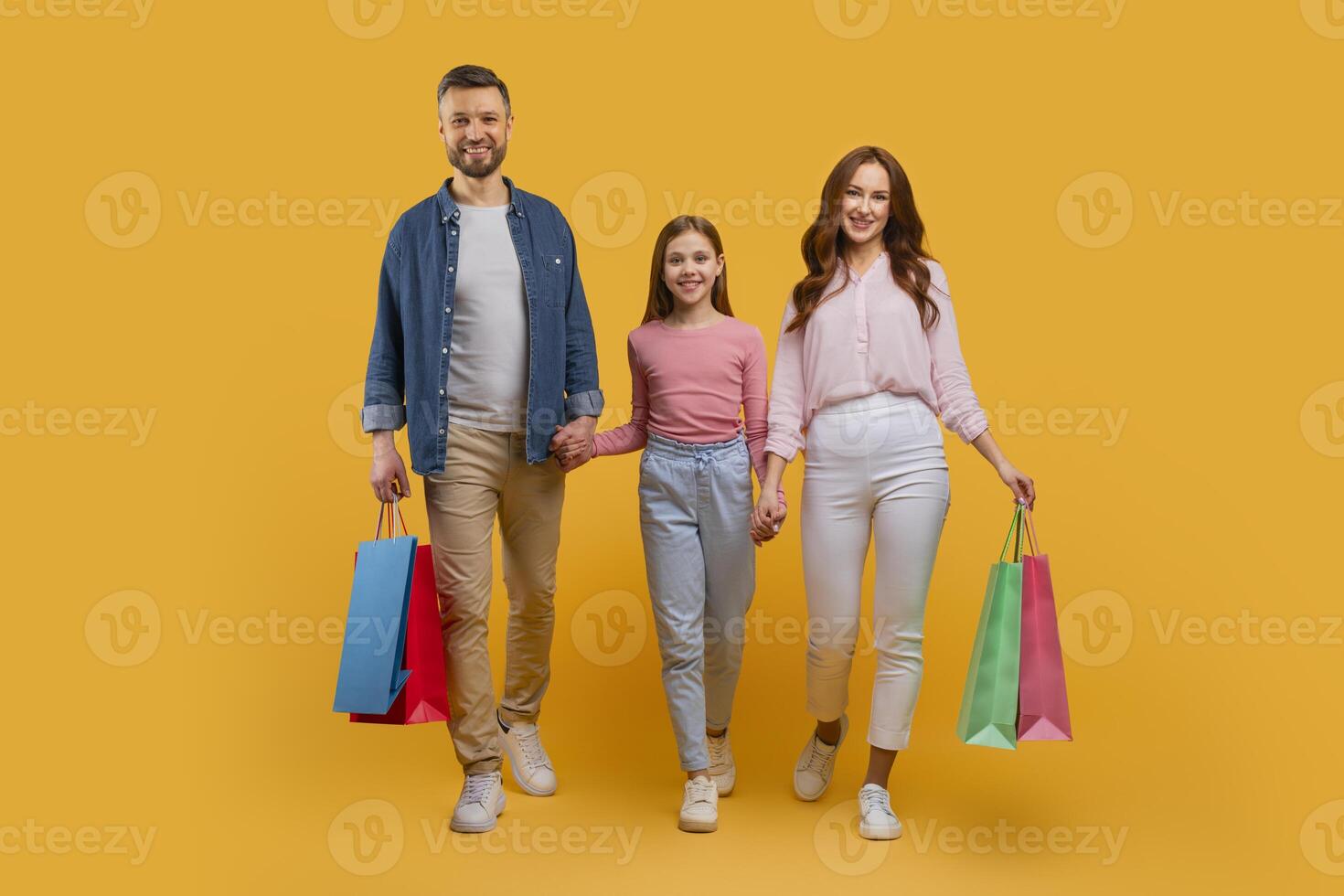 A happy family consisting of a father, mother, and their young daughter are walking side by side, holding colorful shopping bags photo