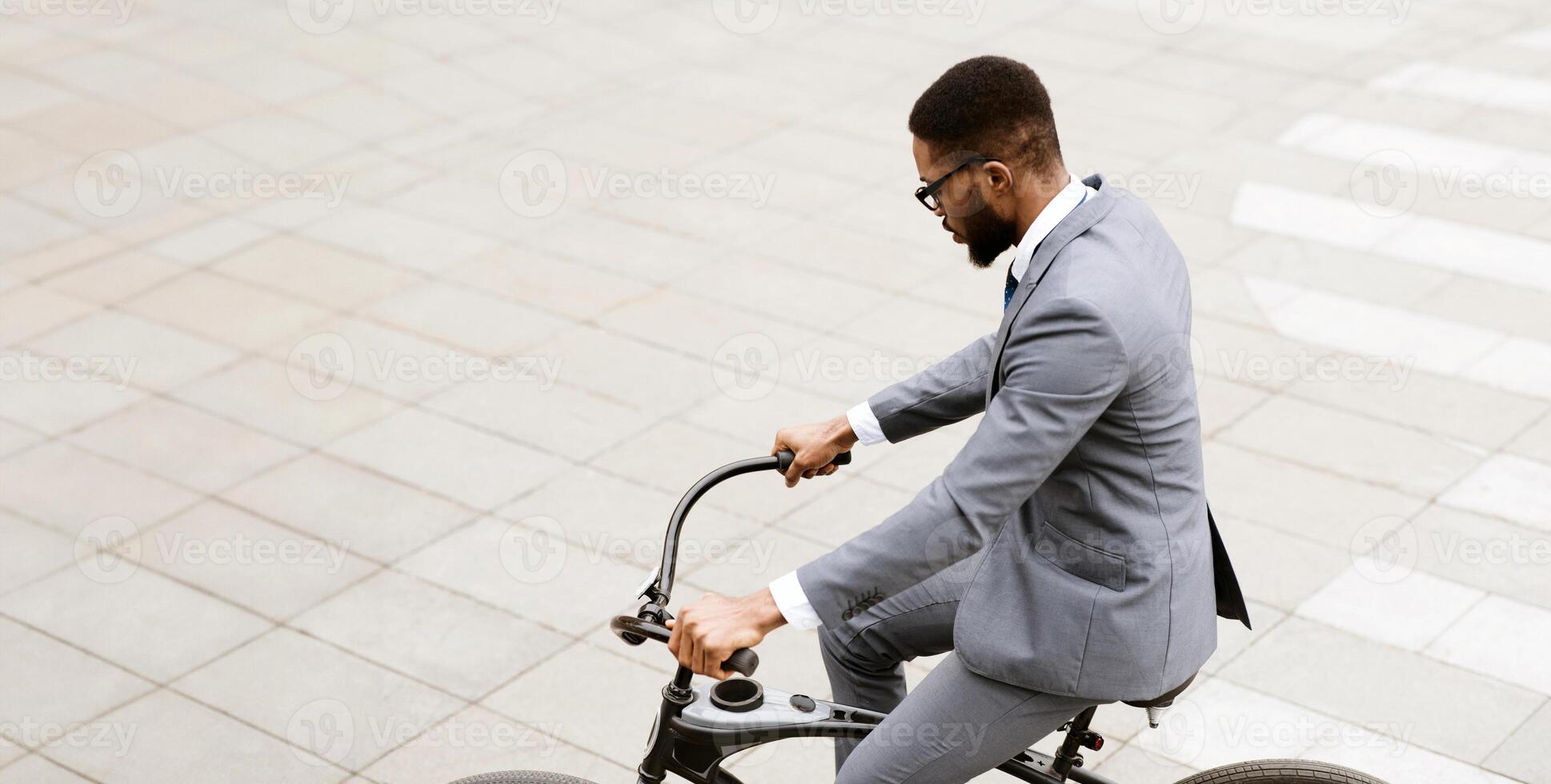 An executive black guy is commuting by bicycle in a cityscape. The mood is energetic and productive, with a focus on a healthy and efficient mode of transportation. photo