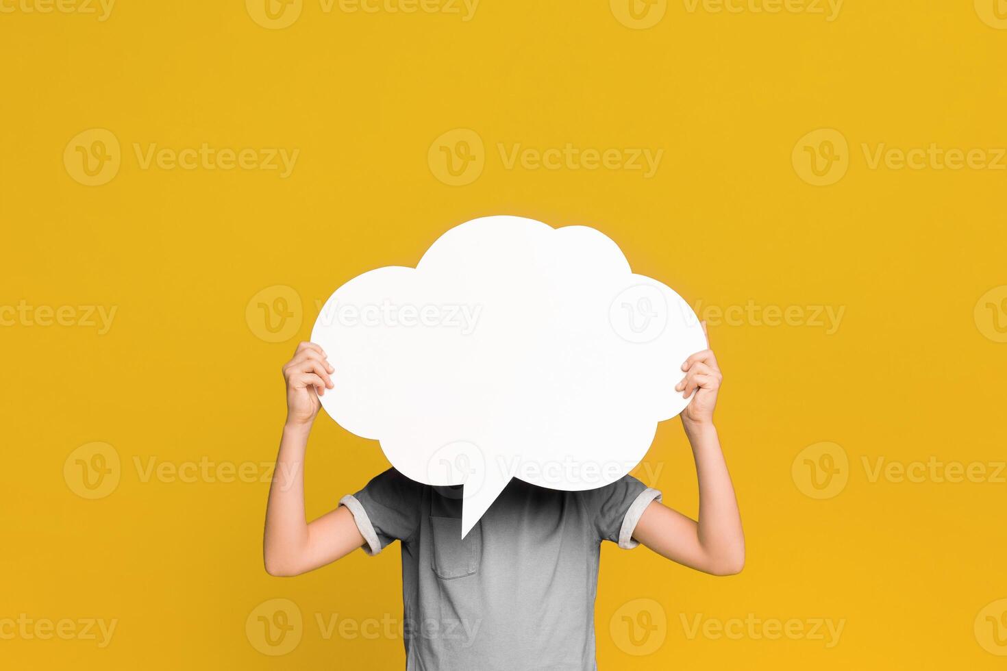 Little boy holding an empty speech bubble in front of his head, orange studio background, free space photo