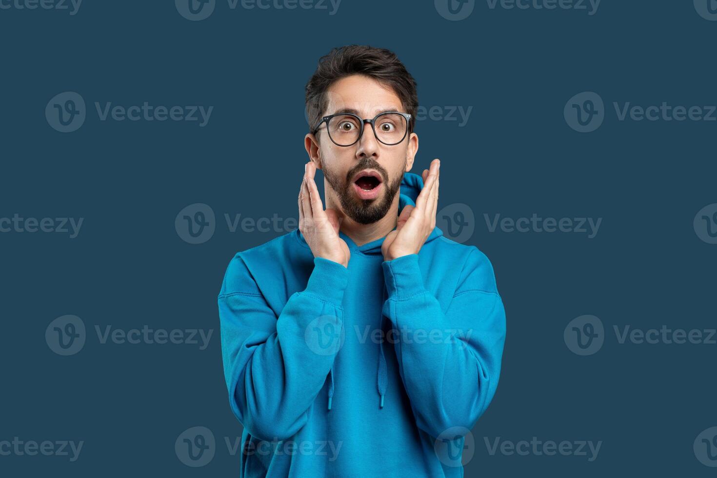 A man wearing glasses with a surprised expression on his face. His eyes widen, eyebrows raise, and mouth forms an O shape in astonishment. The man appears shocked or startled by something unexpected. photo
