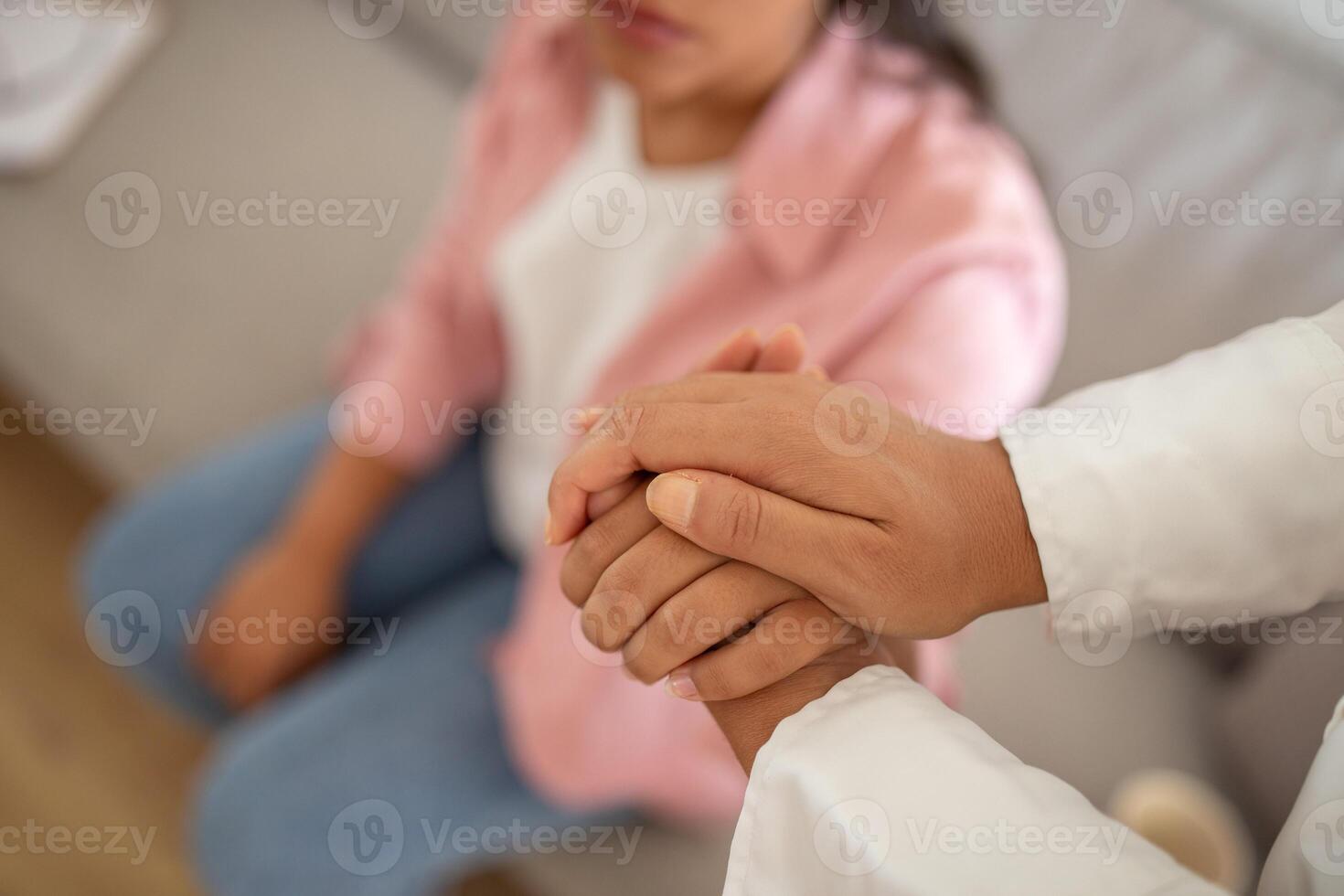 A close up shot showing the hands of a therapist and a patient holding each other. The patients hand is visible in the foreground and is being held by the therapists hand. photo