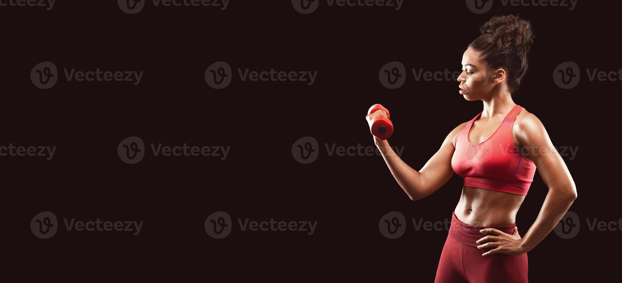 Motivated athletic afro girl working out with fitness dumbbell over black background, free space photo