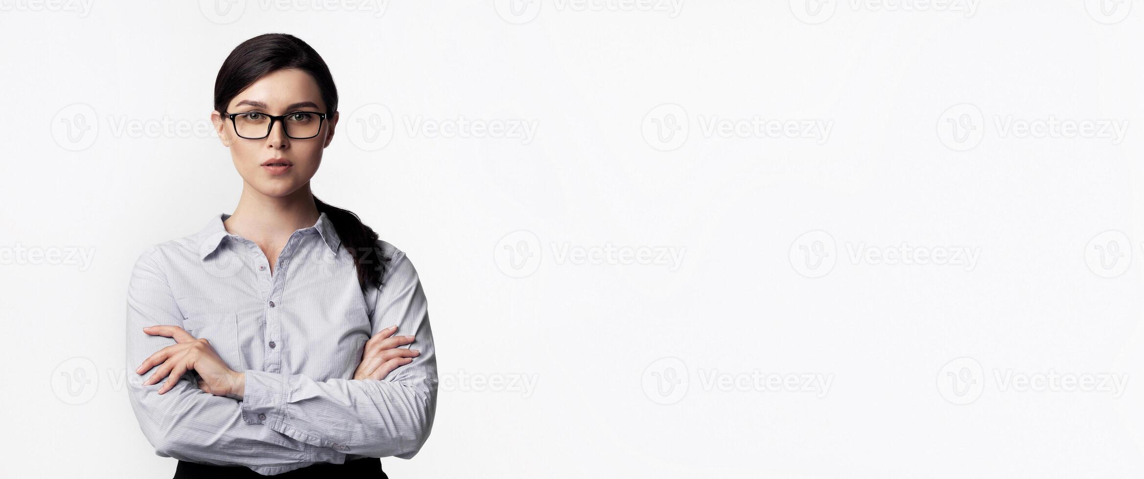 A woman with dark hair, wearing glasses, stands with her arms crossed against a white background. photo