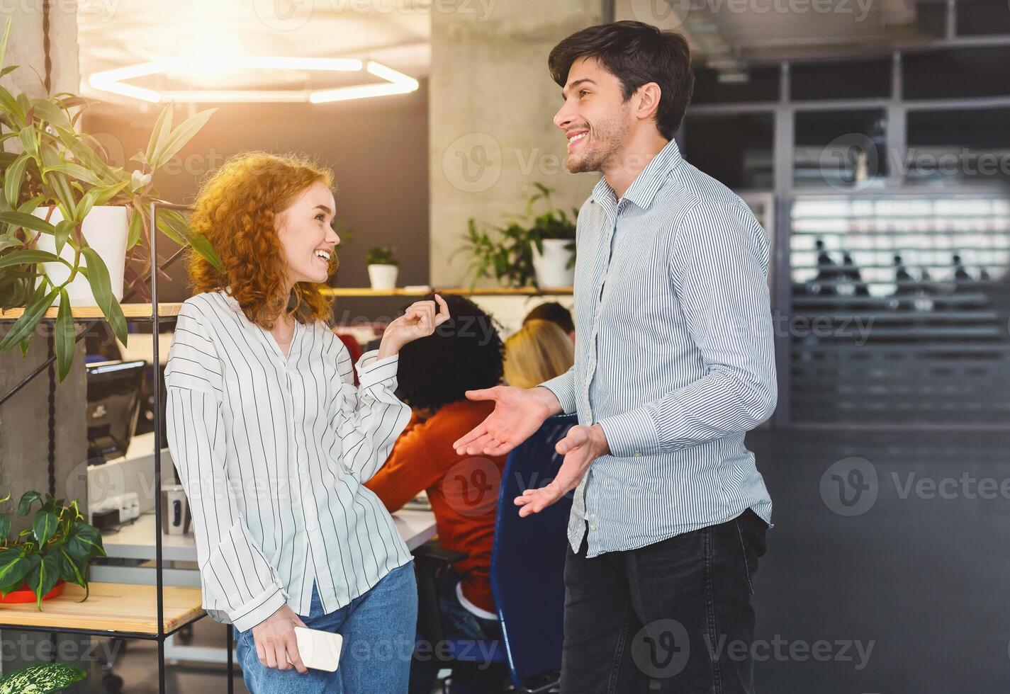 A man and a woman are standing next to each other in a professional office setting. They appear to be engaged in a conversation or discussing work-related matters. photo