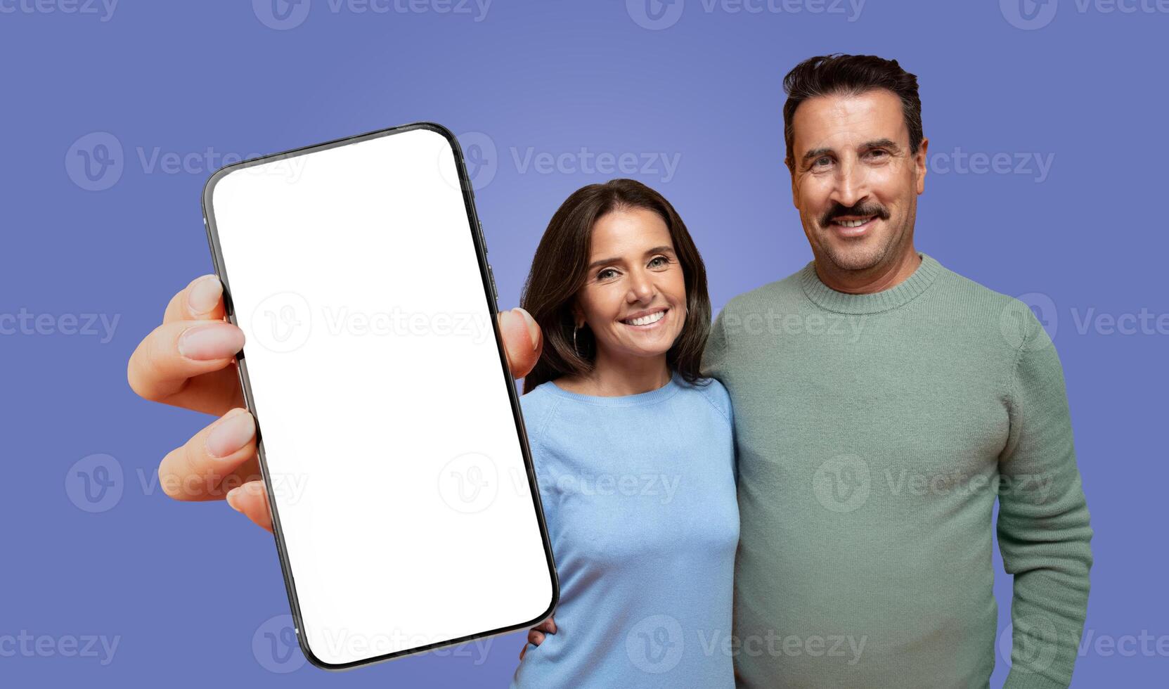 Mature couple stands against a purple background with a hand holding a smartphone with a blank screen towards the camera. photo