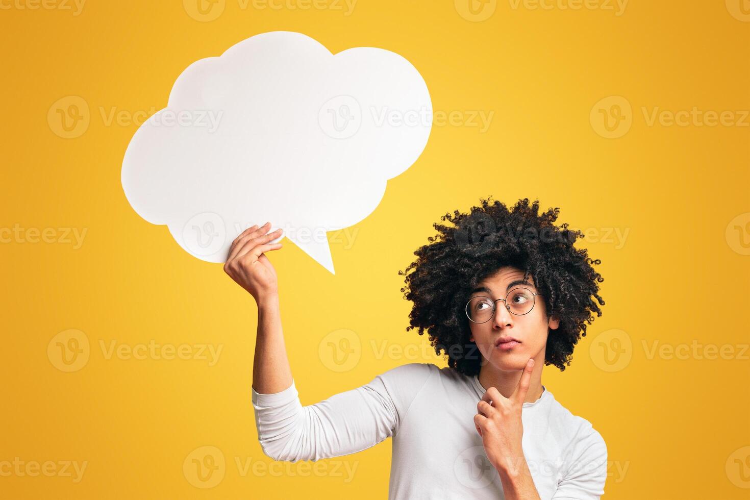 Pensive african-american guy holding blank speech bubble above head and touching his chin, orange background, free space photo