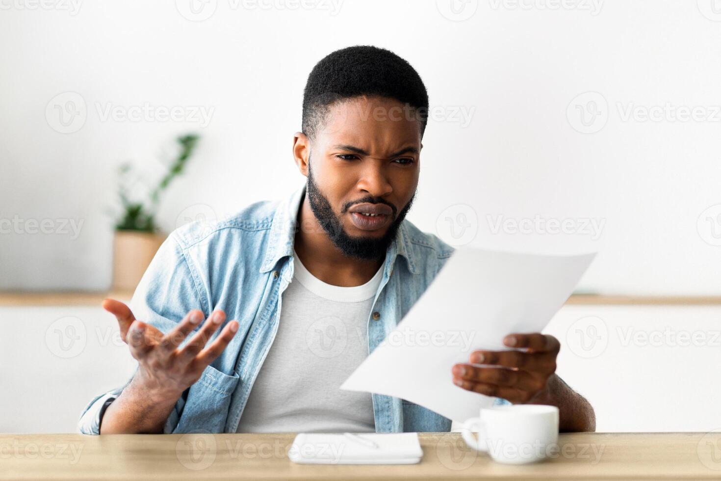 A man sits at a desk and looks surprised, reacting to a piece of paper he is holding. photo