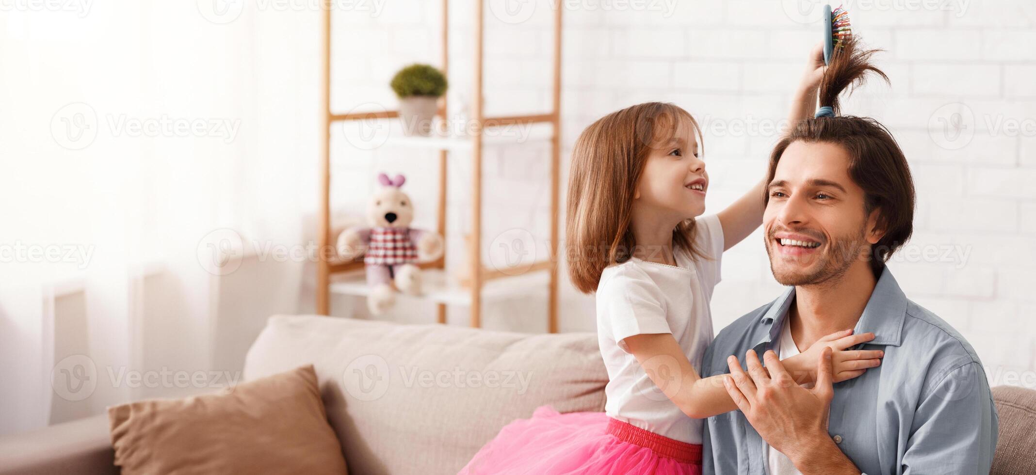 Pretty little daughter combing father hair, brushing and making horse tail, having fun together at home, copy space photo