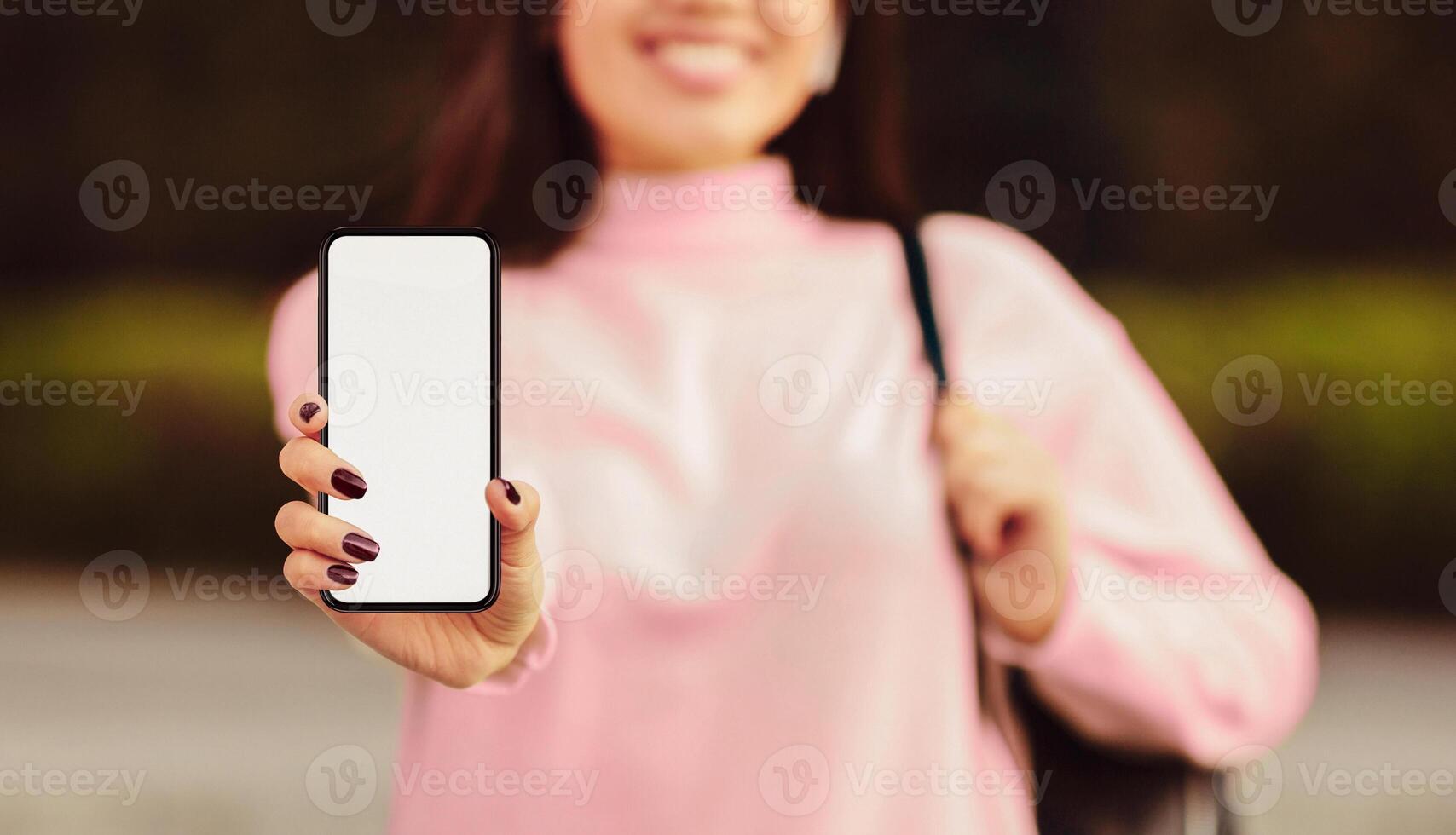 A woman is holding a cell phone in her hand, looking at the screen with a focused expression. She appears to be scrolling or texting, engaged with the device, cropped photo