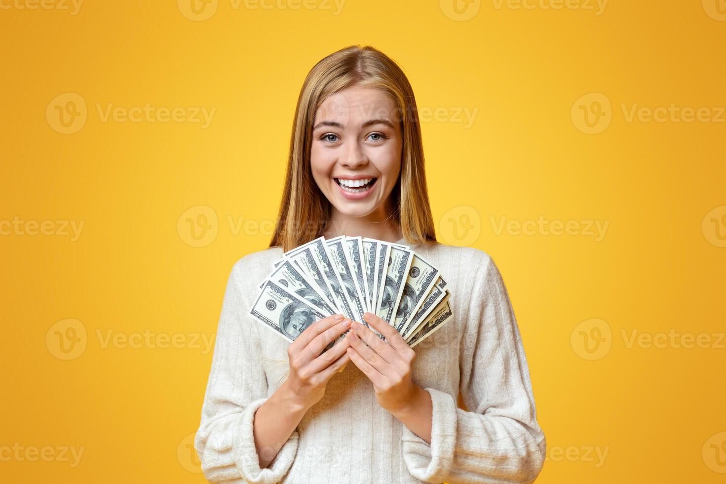 Smart savings. Joyful young girl holding fan of dollars in hands and smiling to camera over orange studio background, copy space photo
