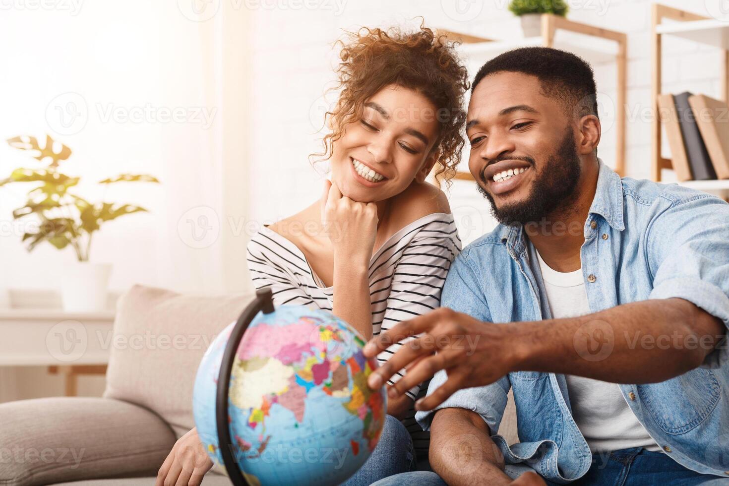 African American man and woman are sitting comfortably on a couch, attentively examining a globe placed between them. They seem engrossed in studying the geography displayed on the globe. photo