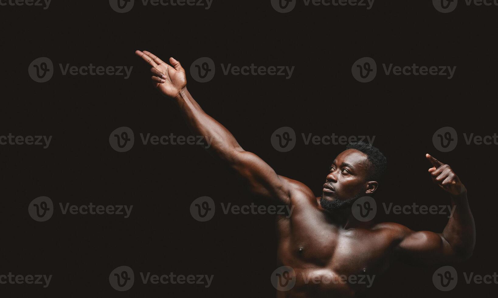 A muscular man poses with his arms raised against a black background. photo