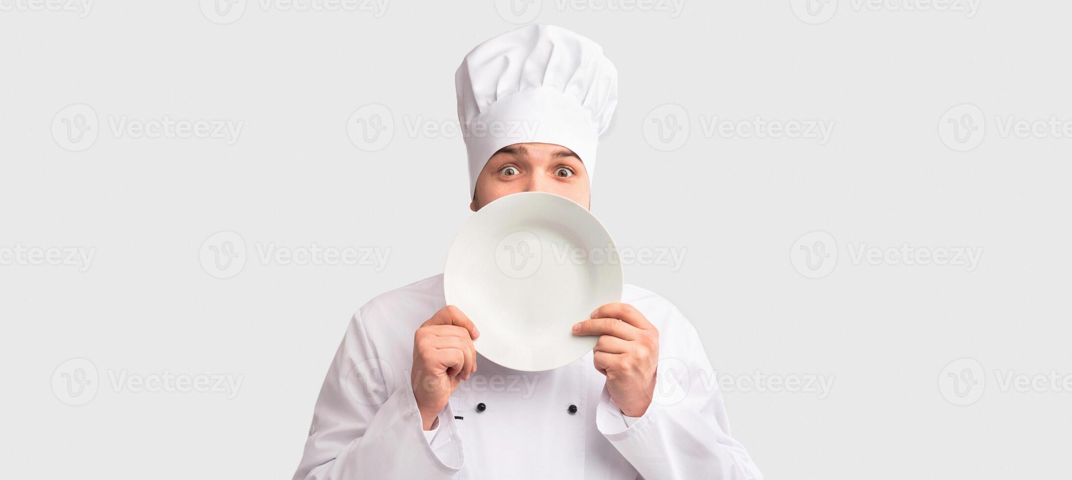 Chef Cook Man Peeking Out Holding Plate Near Face Standing Over White Studio Background. Panorama photo