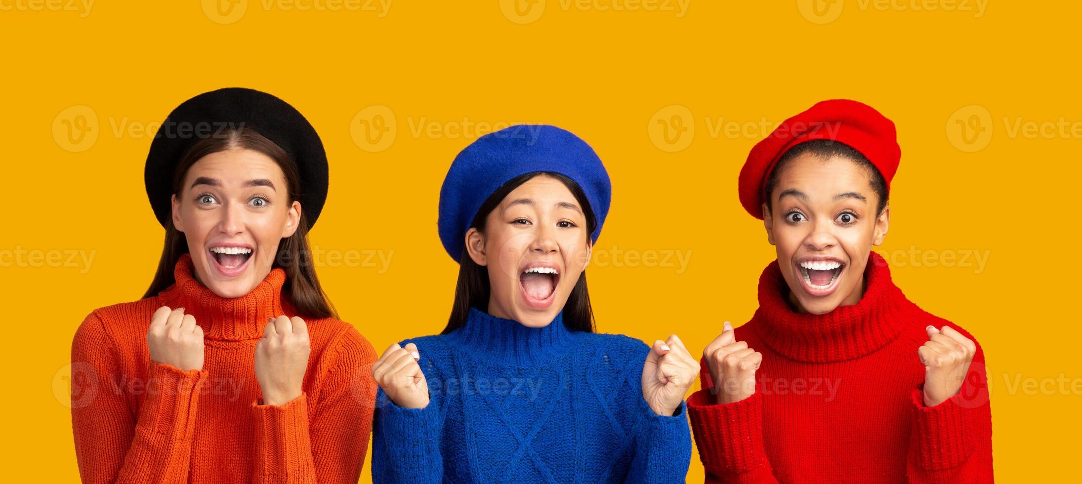 Joy. Excited Diverse Girls In Colorful Sweaters Shaking Fists Gesturing Yes Celebrating Victory Over Yellow Studio Background. Panorama photo