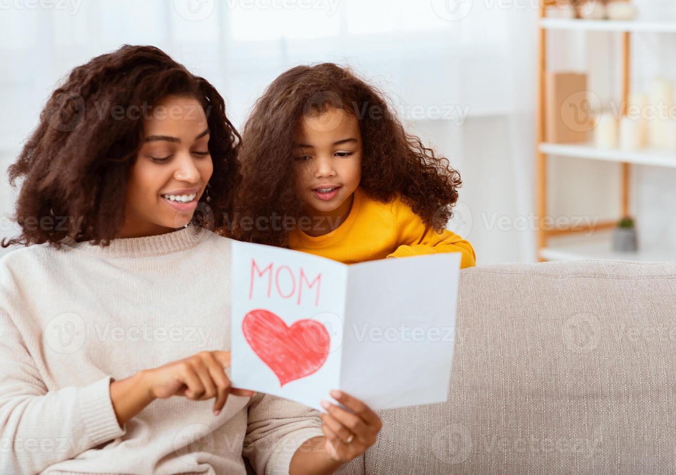 Little Daughter Congratulating Mom On Mother's Day Giving Her Greeting Card Sitting Together On Sofa At Home. Free Space photo