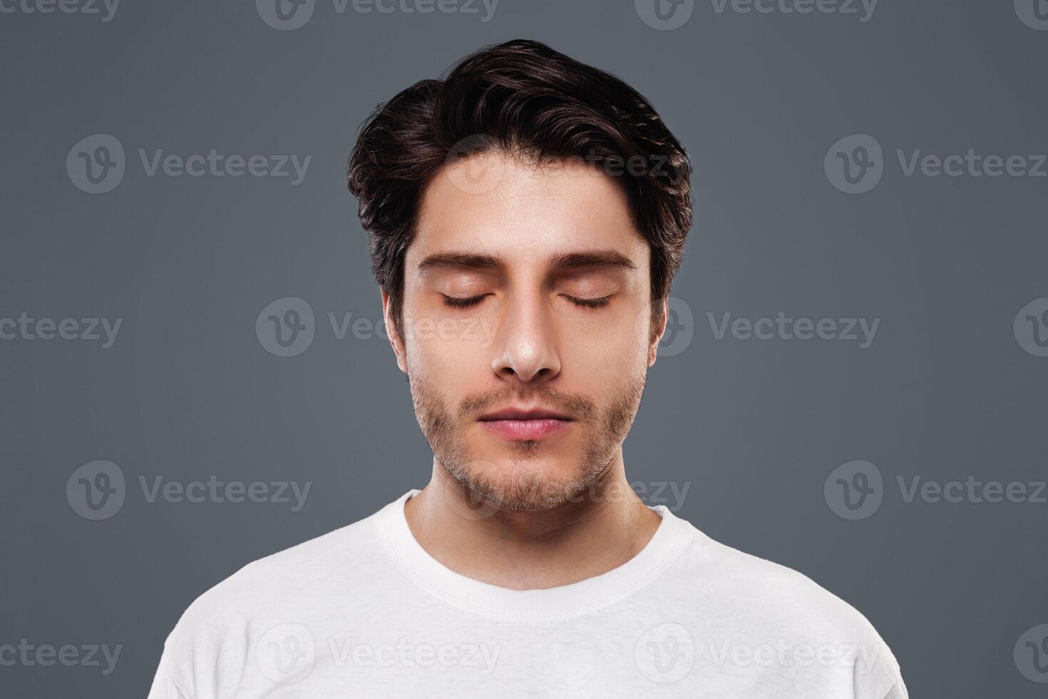 Portrait of handsome millennial man with closed eyes, grey studio background photo