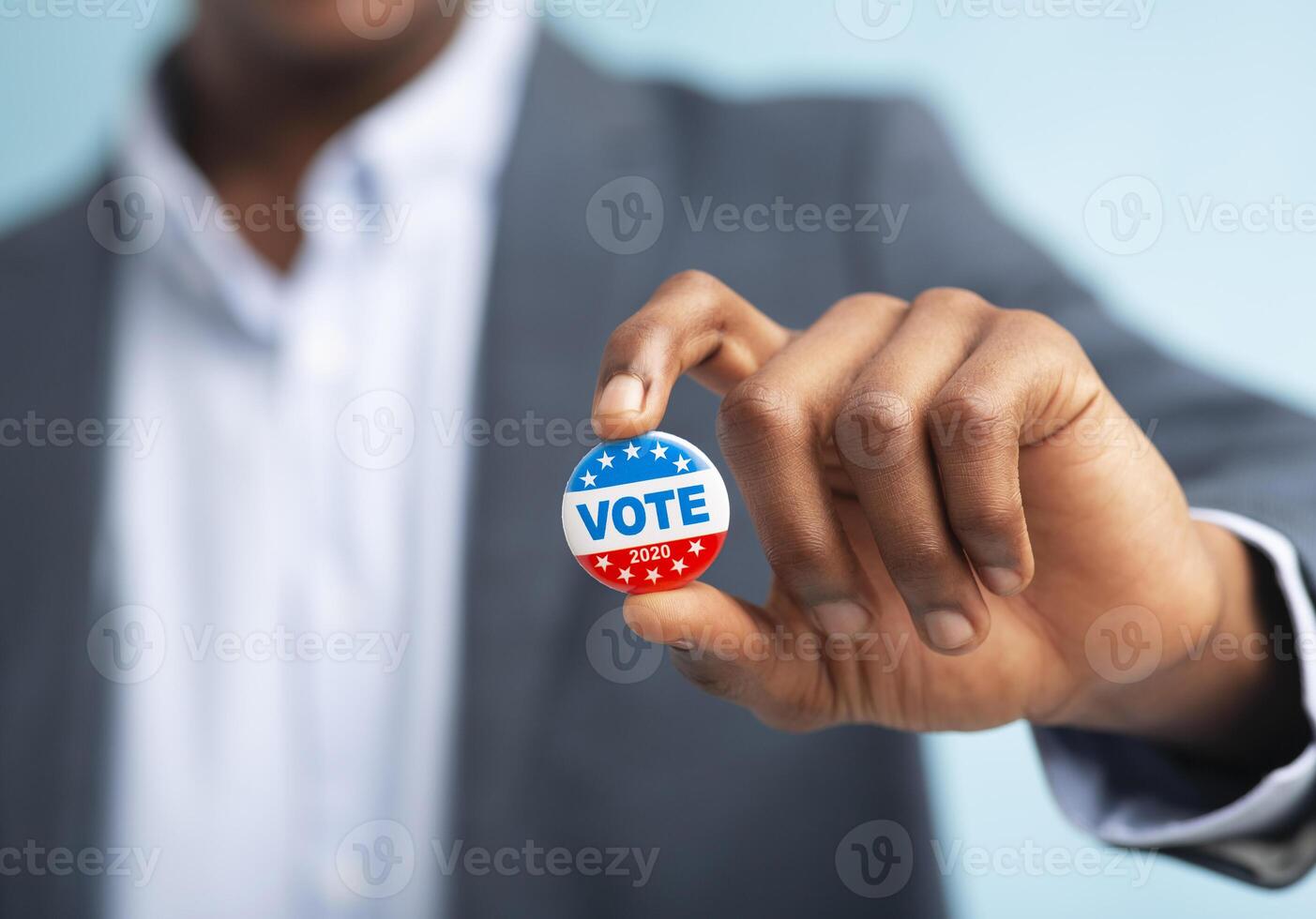 African man holding vote button on blue background for the November elections in the United States 2020, blurred photo