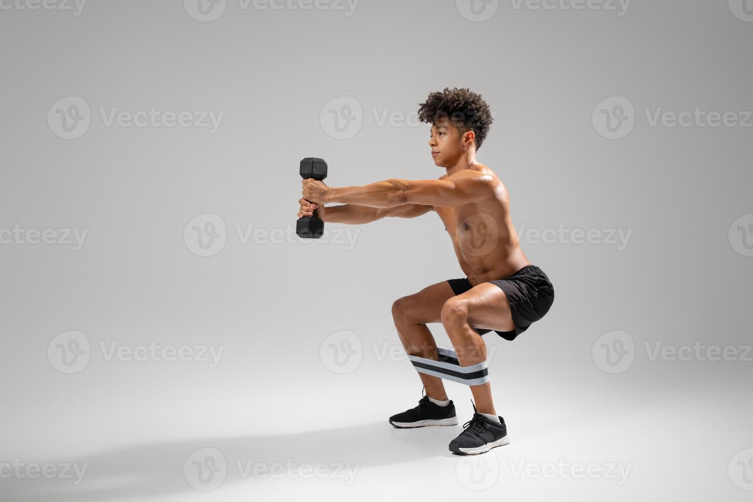 A young man engages in a strength training exercise involving weighted squats while using a dumbbell. He focuses on maintaining proper form as he balances on his feet with a resistance band photo
