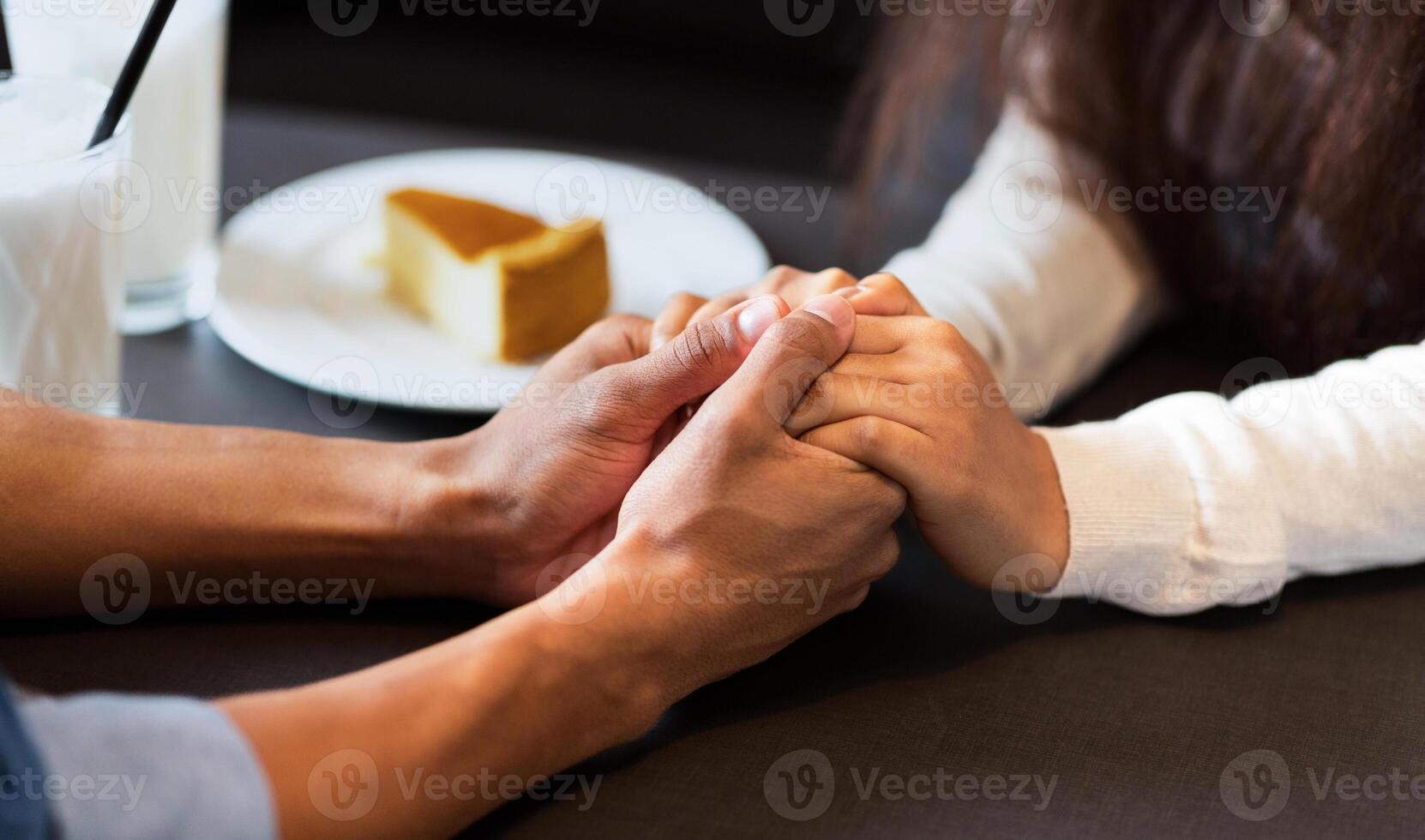 Cropped of a guy and a girl are seated at a table, holding hands. They appear to be engaged in a conversation. photo