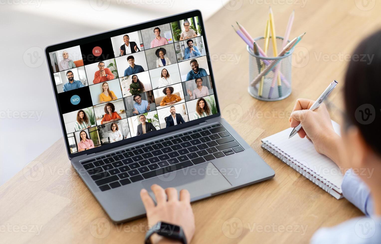 Woman manager sits at a wooden desk with a laptop computer open in front of them. The screen shows a conference with multiple participants. photo