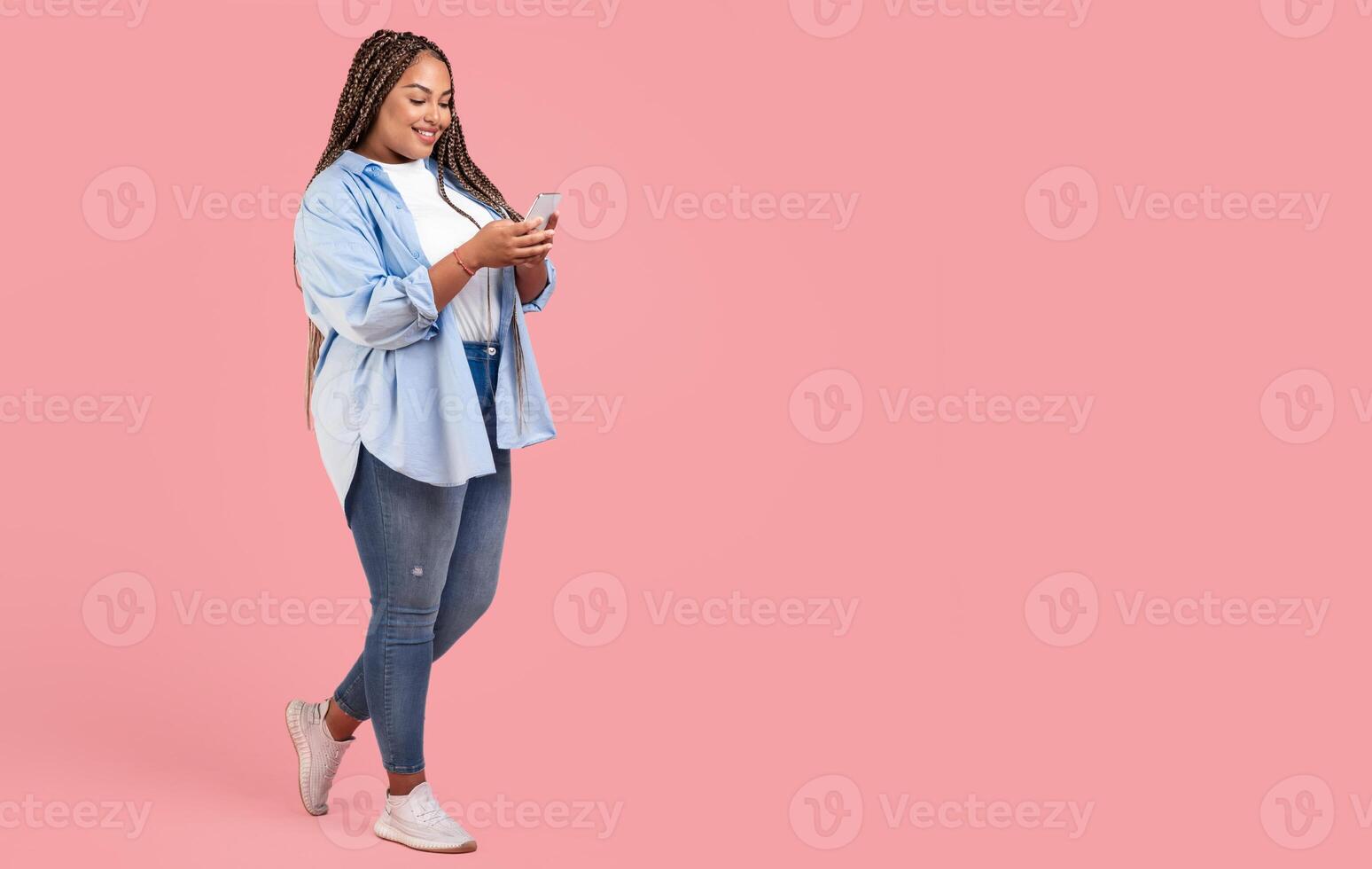 African American Plus Size Female Using Smartphone Texting Standing Posing On Pink Background, Studio Shot. Great Mobile App Concept. Full Length, Copy Space photo