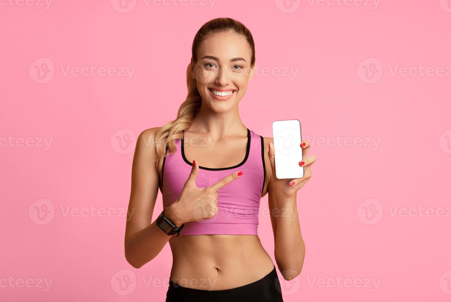 Sport Apps. Fitness Girl Pointing Finger At Cellphone Blank Screen On Yellow Background In Studio. Copy Space, Mockup photo