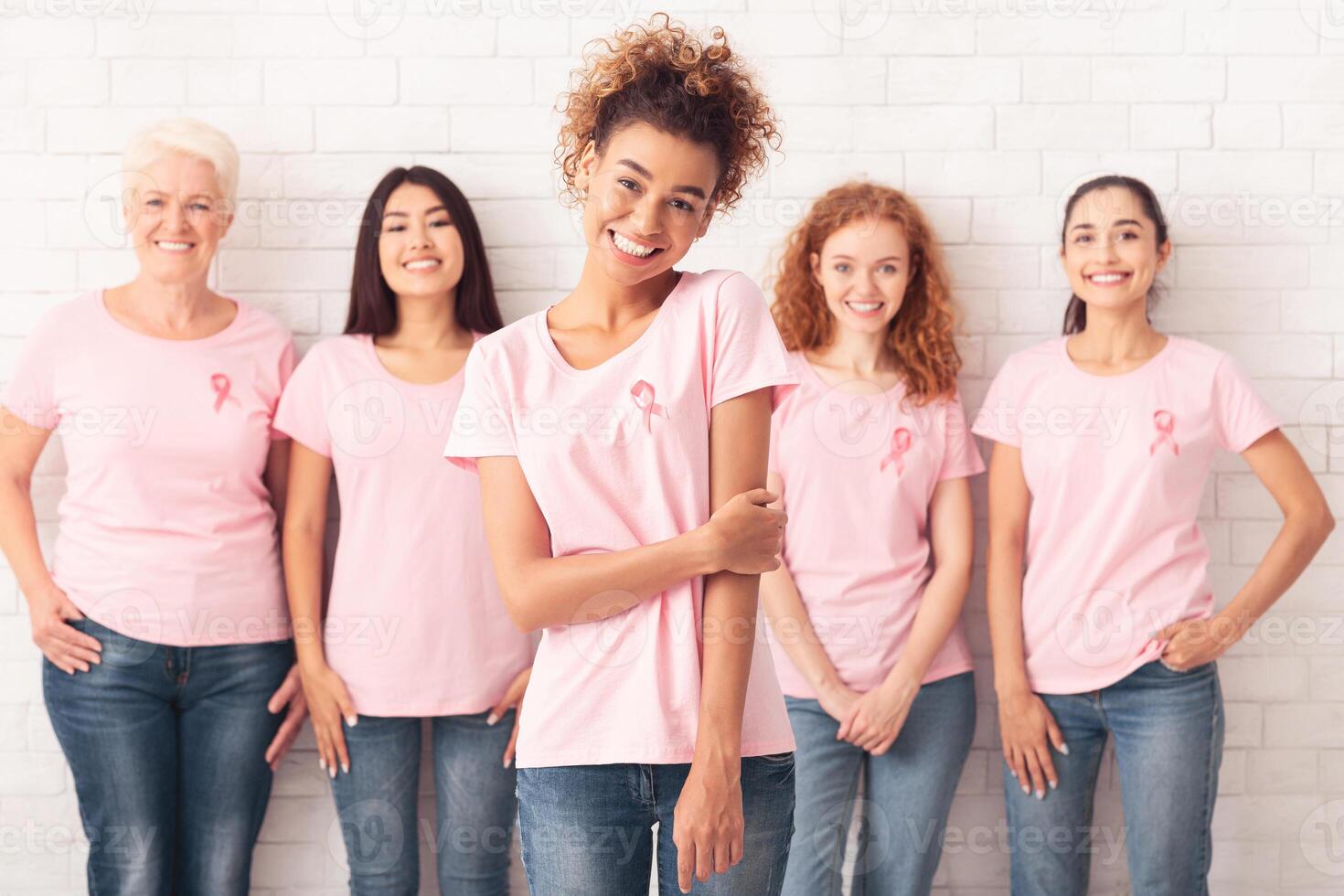 Breast Cancer Support. African Volunteer Girl Wearing T-Shirt With Pink Ribbon Standing With Group Of Diverse Volunteers On White Background photo