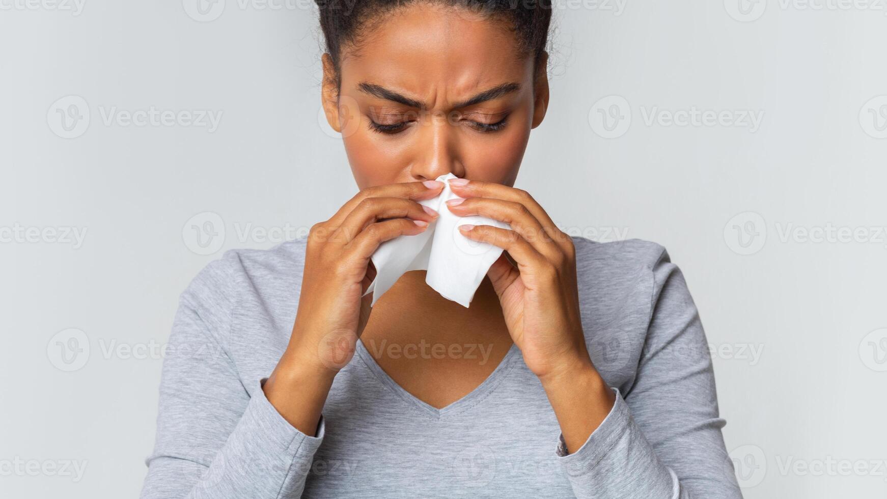 Black girl touching her nose with napkin, having runny nose, grey background photo