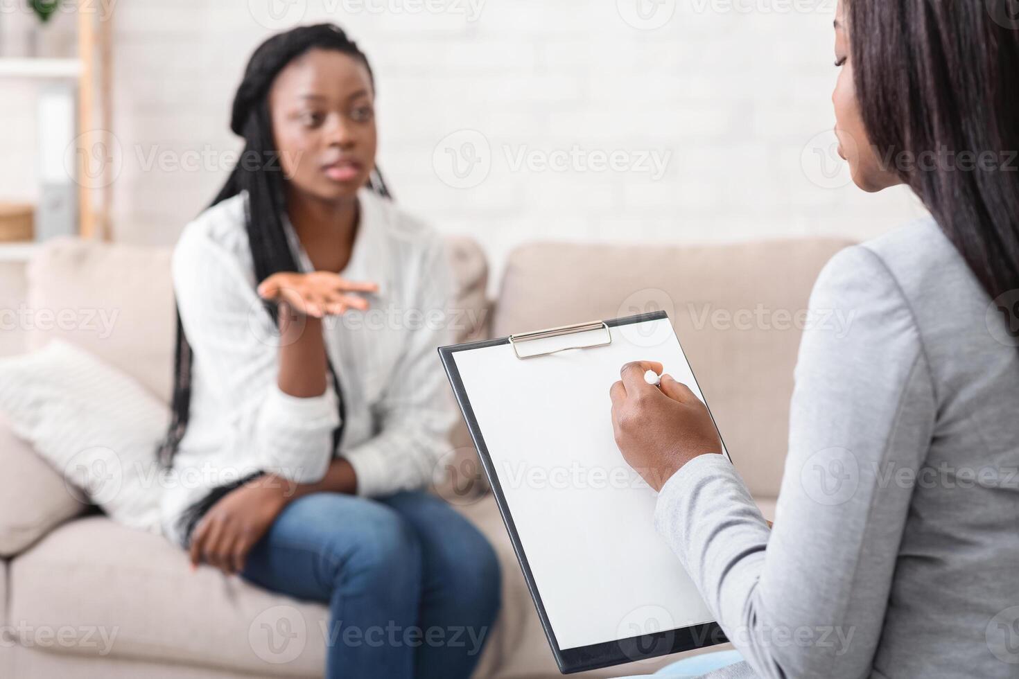 Psychologist taking notes during therapy session with her emotional female patient that talking with about her problems and actively gesturing photo