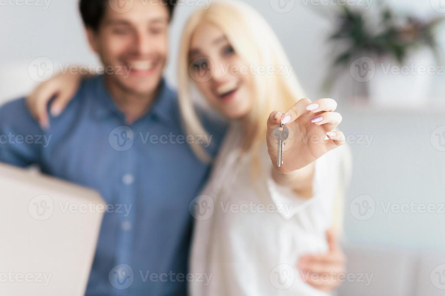 A happy couple stands together, the woman holding keys to their new home. photo