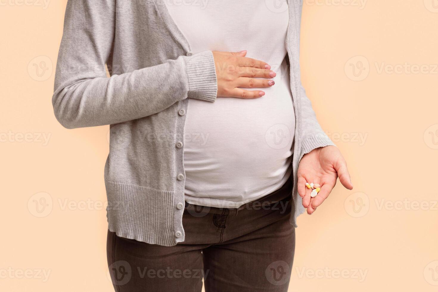 Medicines During Pregnancy. Unrecognizable Pregnant Woman Showing Pills In Hand Touching Belly Standing On White Background In Studio. Cropped photo