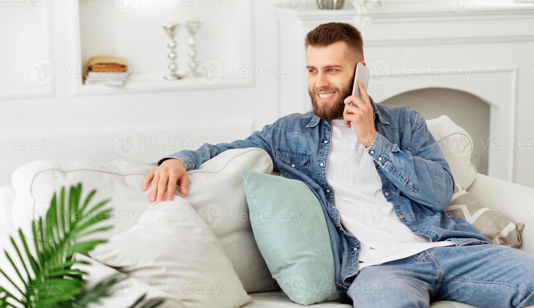 A man is seated on a couch, engaged in a conversation on his cell phone. photo