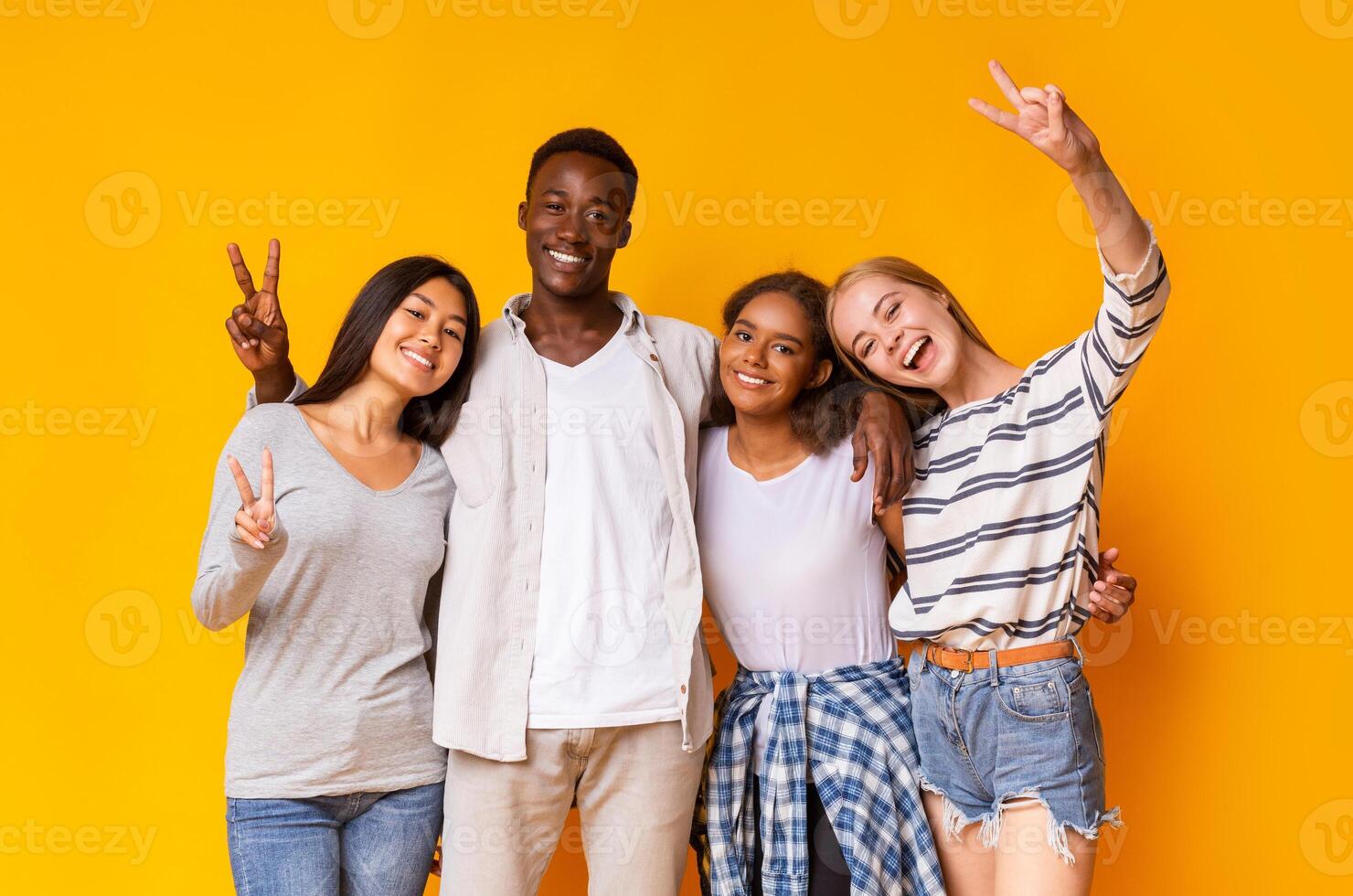 Carefree mixed race students having fun over yellow background, showing peace gesture photo