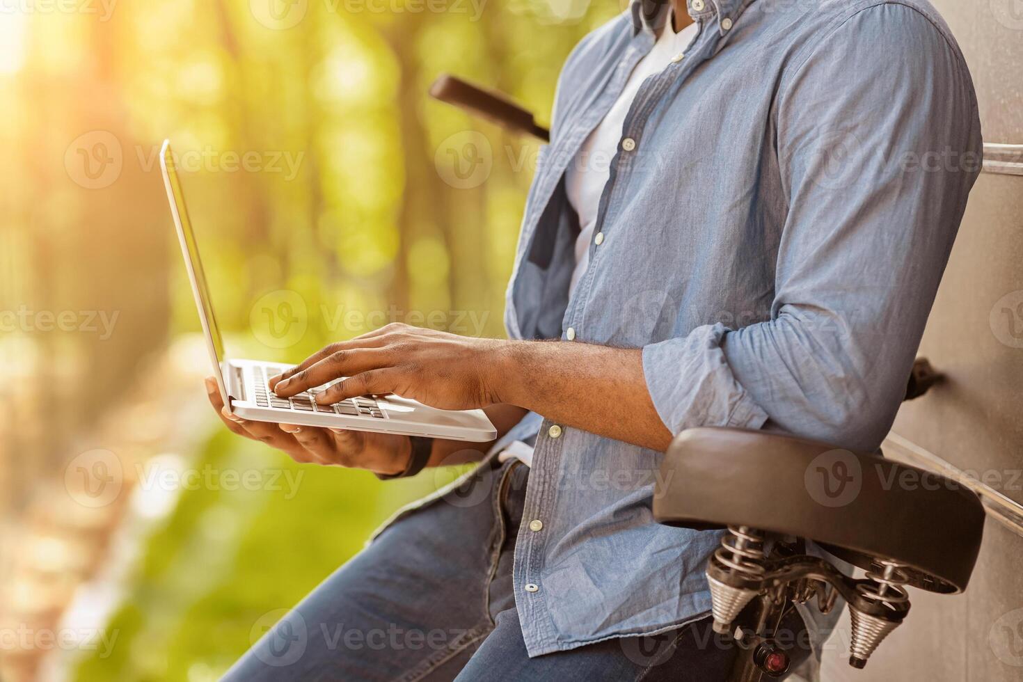 Unrecognizable black man leaning on bicycle and using laptop outdoors, side view, cropped image with free space photo