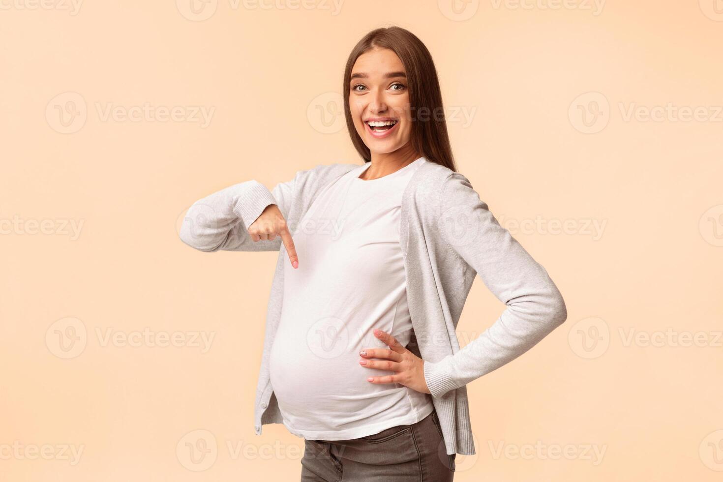 Pregnancy. Happy Pregnant Woman Pointing Finger At Belly Standing Over White Studio Background. Copy Space photo