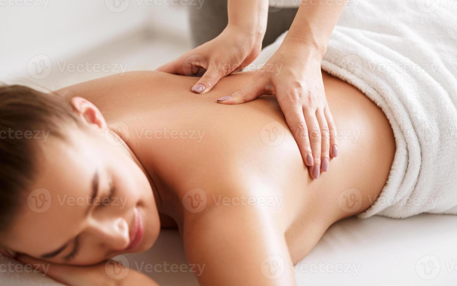 Young girl receiving back massage with closed eyes in spa center, closeup photo