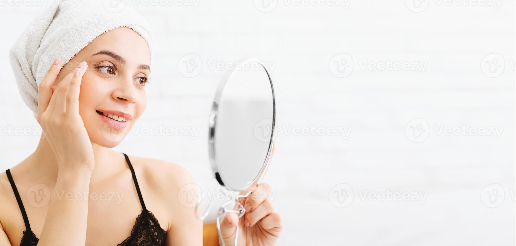 A woman is holding a mirror while a towel is wrapped around her head. She appears to be looking at her reflection in the mirror. photo