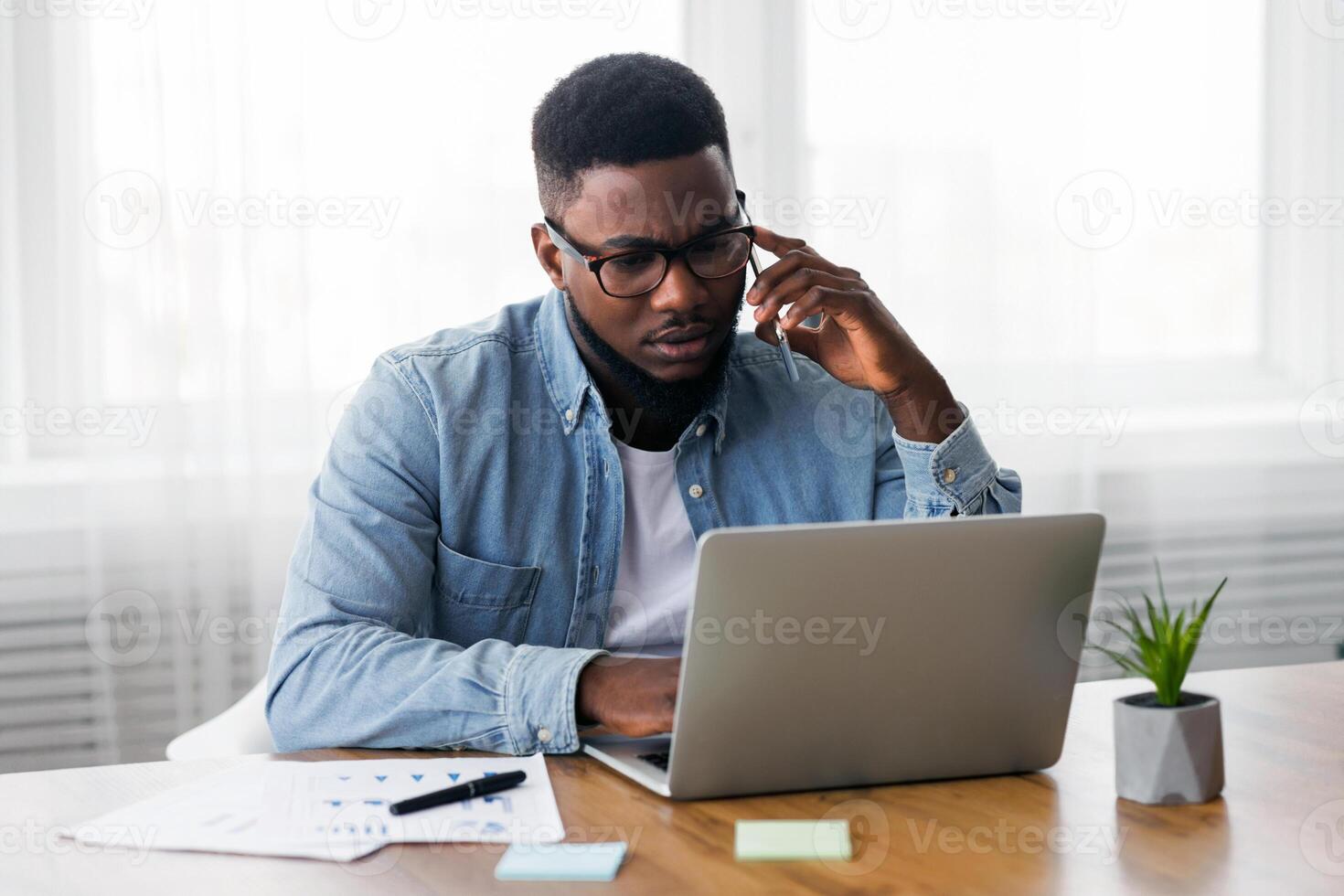 Concerned african american employee talking on mobile phone and looking at laptop screen, having issues with project, copy space photo
