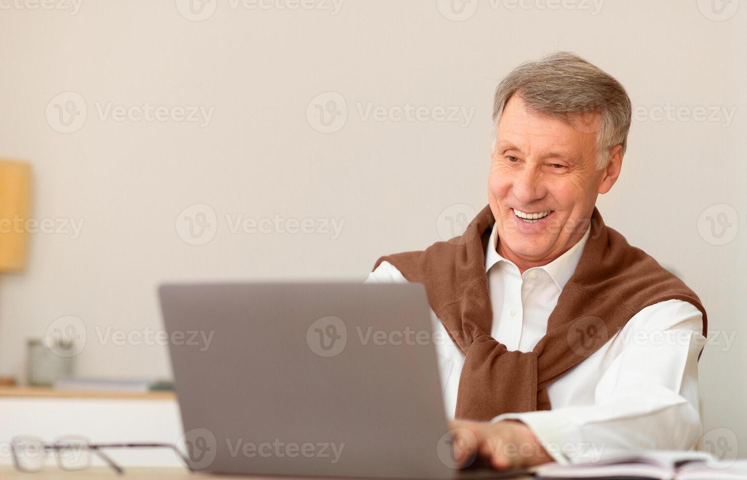 Work In Old Age. Smiling Senior Gentleman Sitting At Laptop Computer In Modern Office. Selective Focus photo